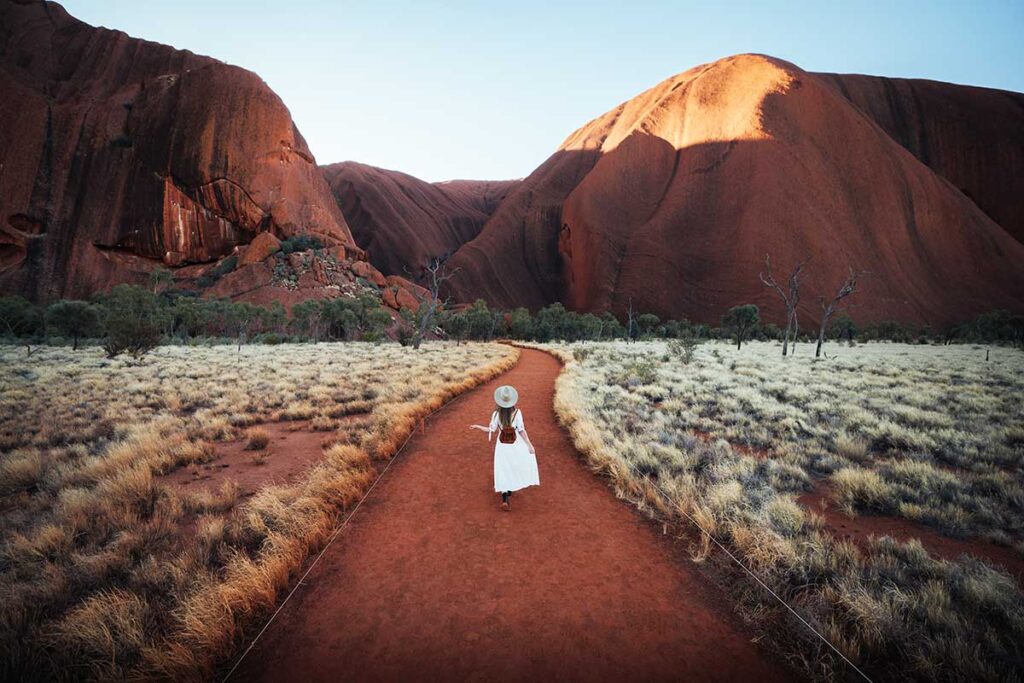 woman walking towards the base of Uluru at sunrise